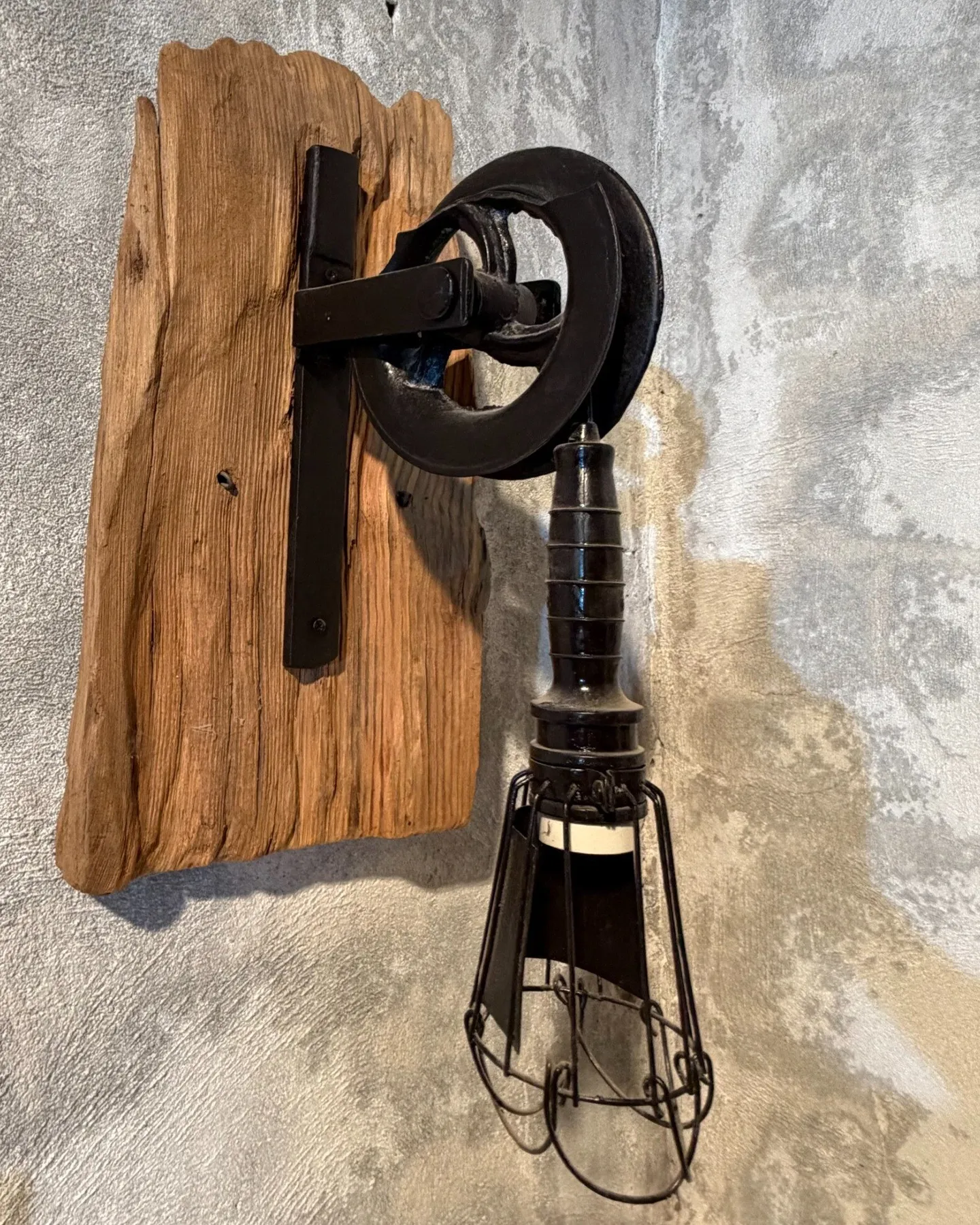 Aplique de pared con una polea de hierro antigua sobre madera y una lámpara de jaula