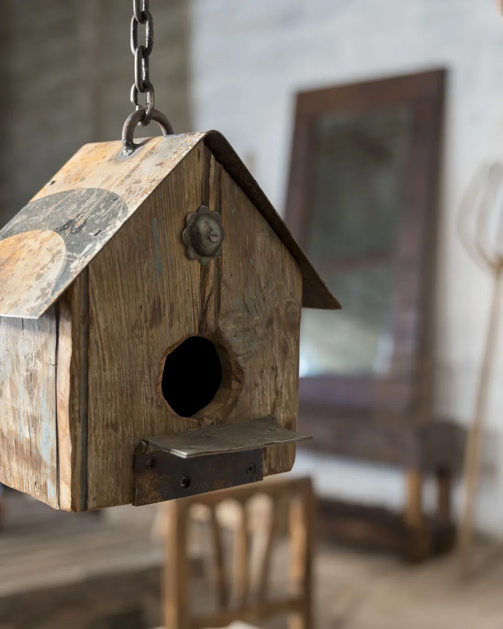Casita de pájaros de madera recuperada con tejado de chapa, colgada de una cadena
