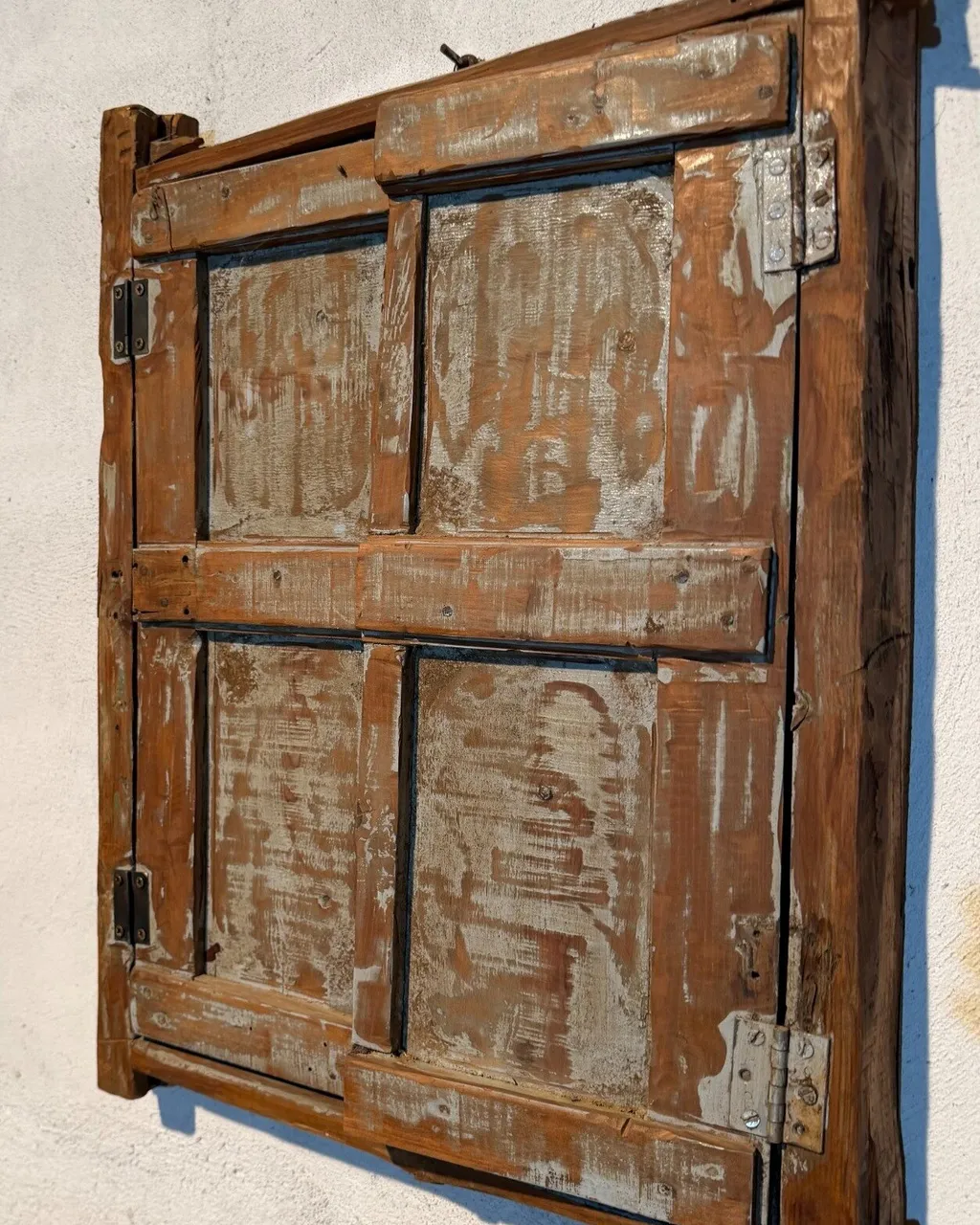 Contraventana antigua de madera con pintura desgastada y bisagras de hierro, colgada en la pared