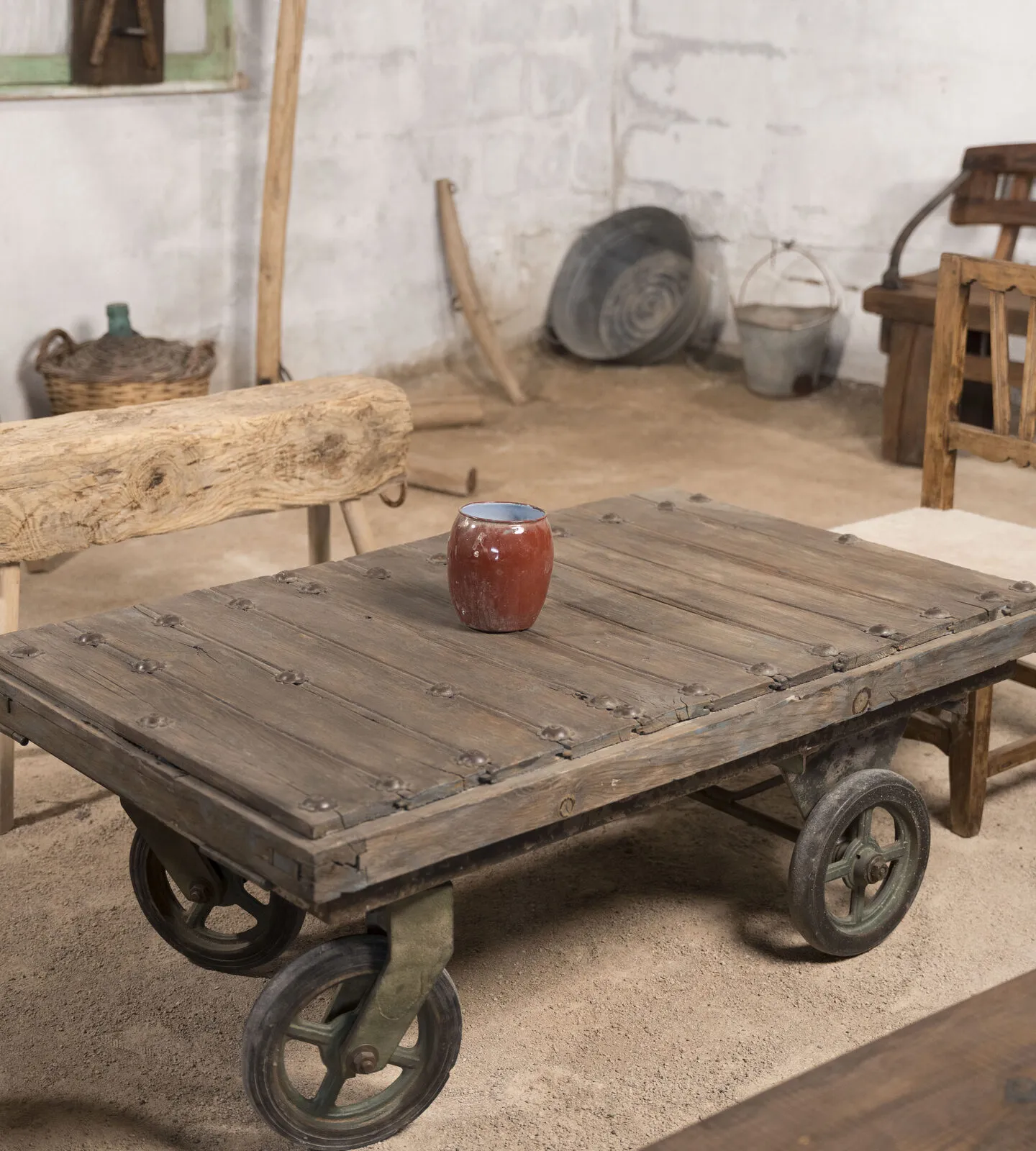 Mesa baja sobre un antiguo carro industrial con ruedas de hierro, con un jarrón rojo encima