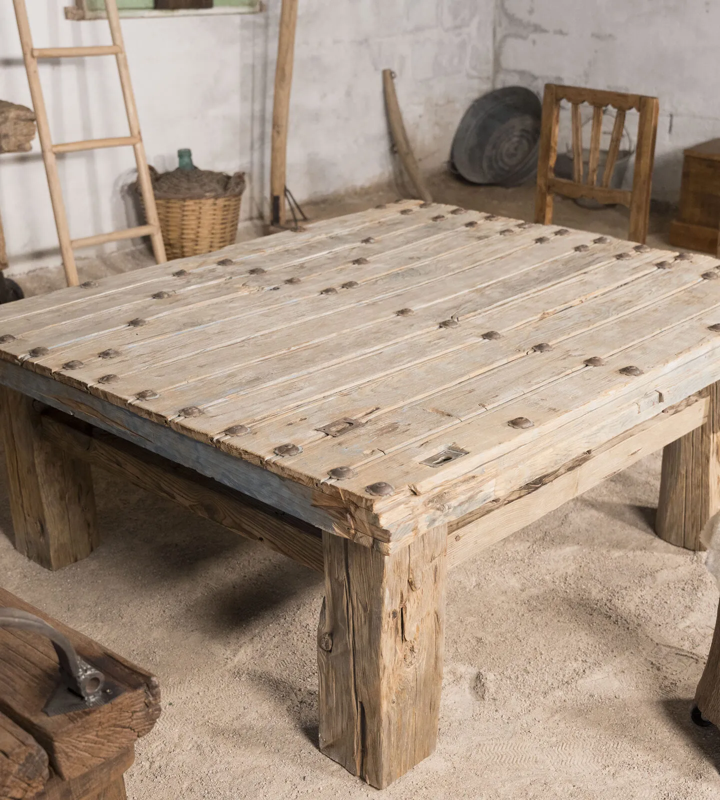 Mesa baja de madera clara con tachuelas de hierro, junto a un taburete de tronco con piel